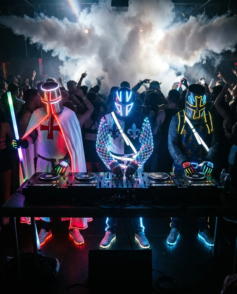 Les chevaliers néon de Sainte Rave derrière un DJ booth, foule en transe dans la fumée et les lasers