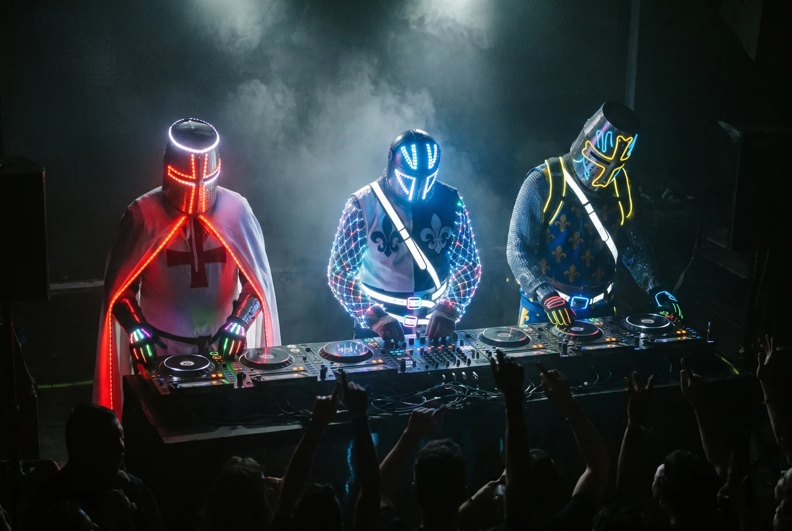 Les chevaliers néon de Sainte Rave au DJ booth en club, foule mains levées dans la fumée